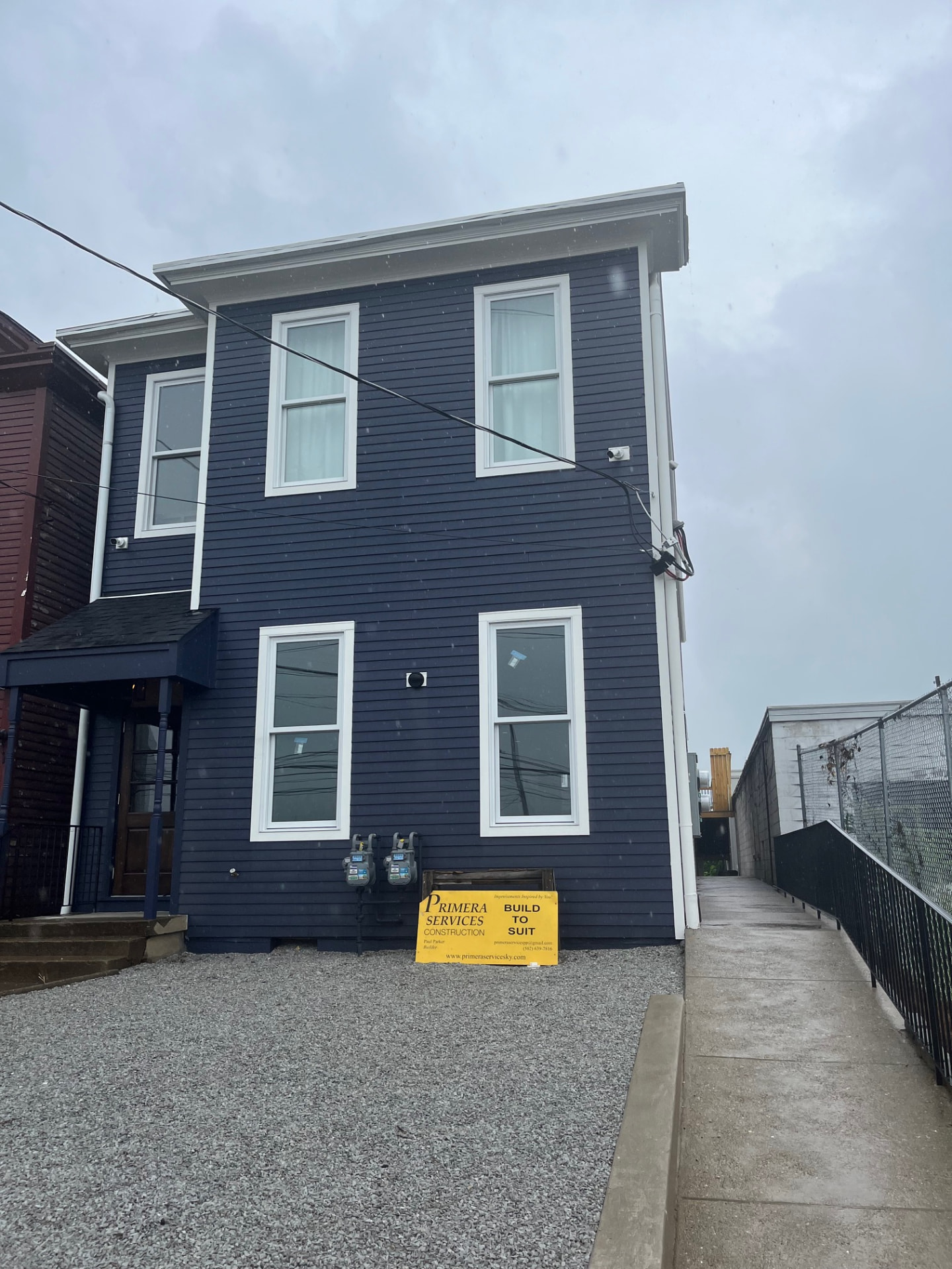 Finished two-story home with navy siding, white trim and a Primera job site sign out front