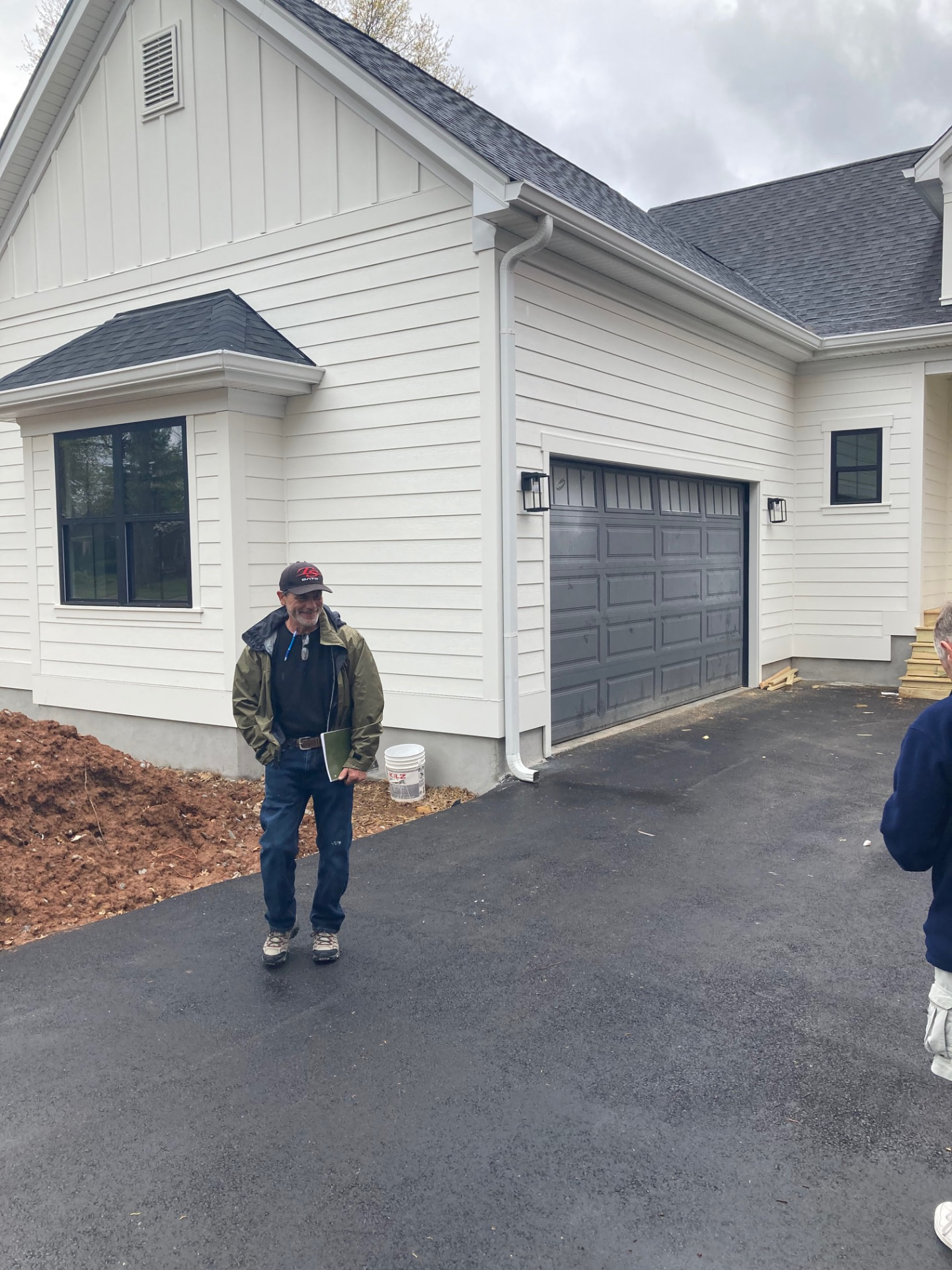 White custom home with board-and-batten gable, dark garage door and a fresh asphalt drive